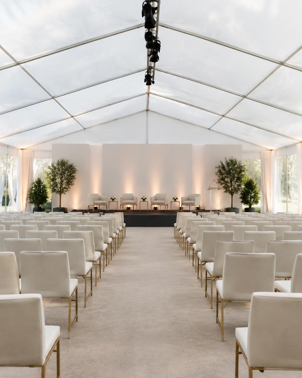 Rows of seating facing a stage inside a bright white clearspan marquee