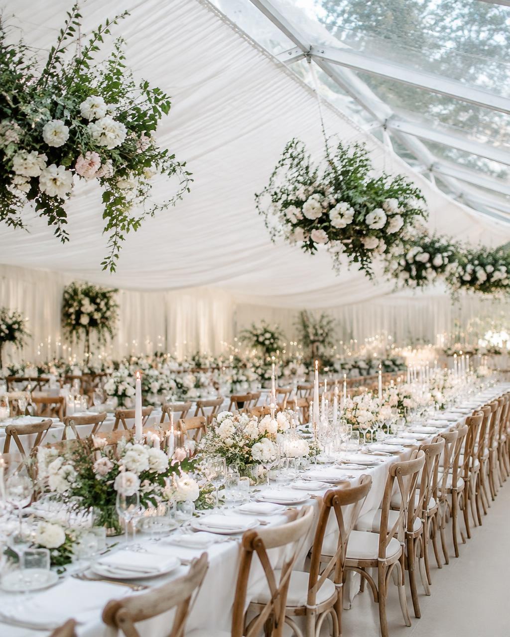 Long dining tables beneath ivory-lined marquee ceiling dressed with hanging florals