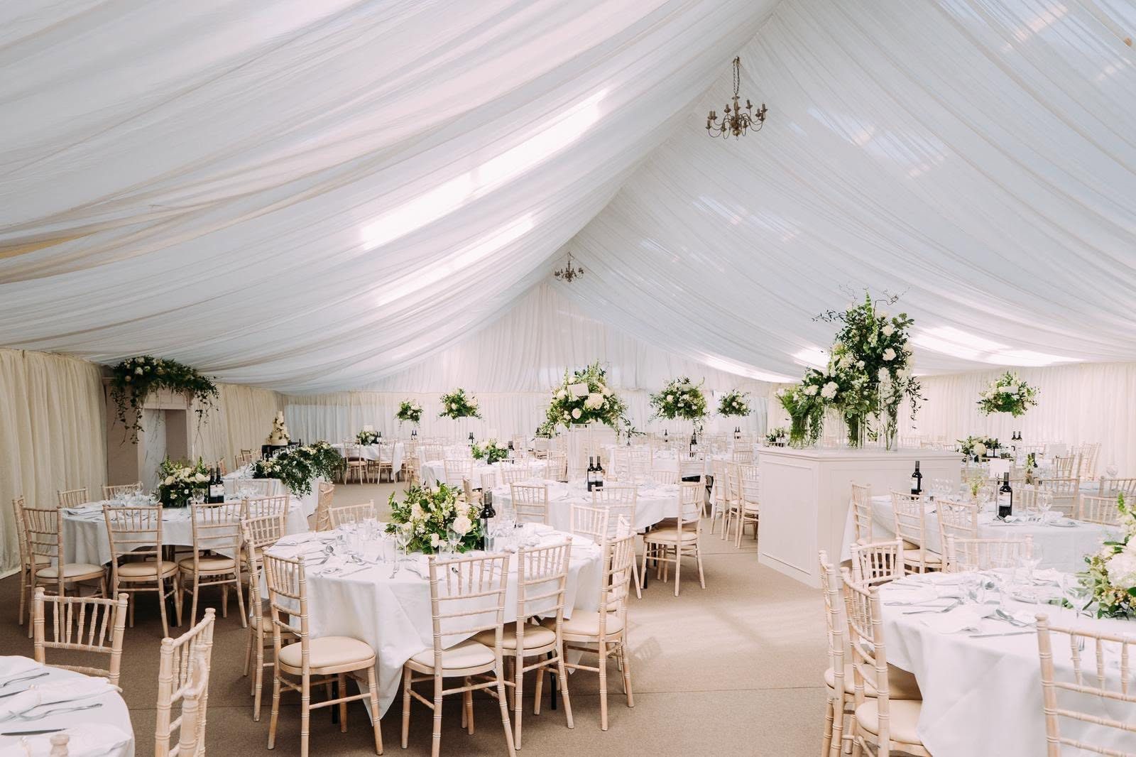 Interior of a DTL marquee with ivory pleated lining, round tables and chandeliers